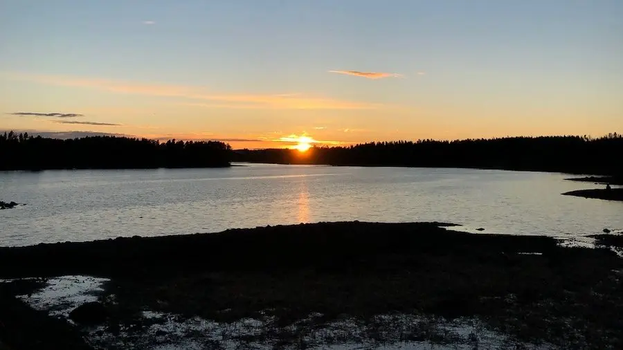 Solnedgång över sjön med skogsklädd strand i Jämtlands län