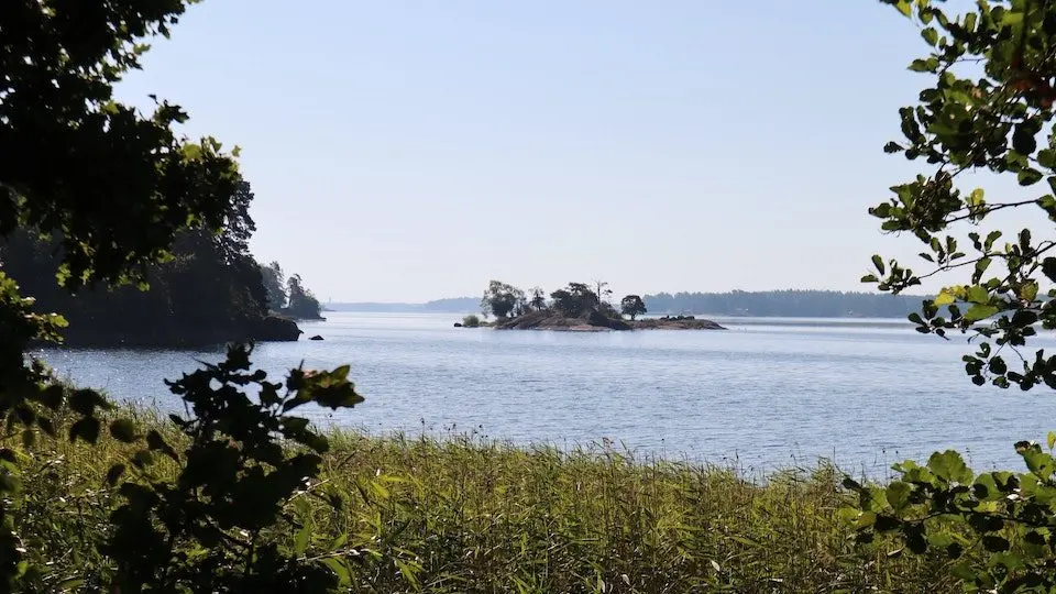 Liten klippig ö i sjön, sedd genom lövverk, Östergötlands län